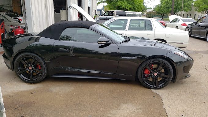 A black convertible sports car with black wheels parked outside a shop beside other vehicles