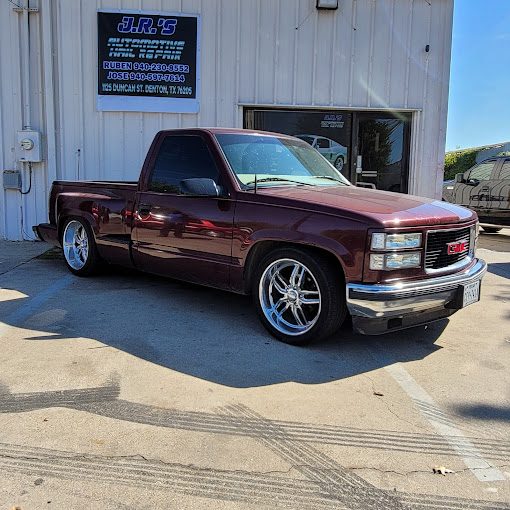 A maroon GMC pickup with chrome wheels parked in front of a metal building with a posted sign