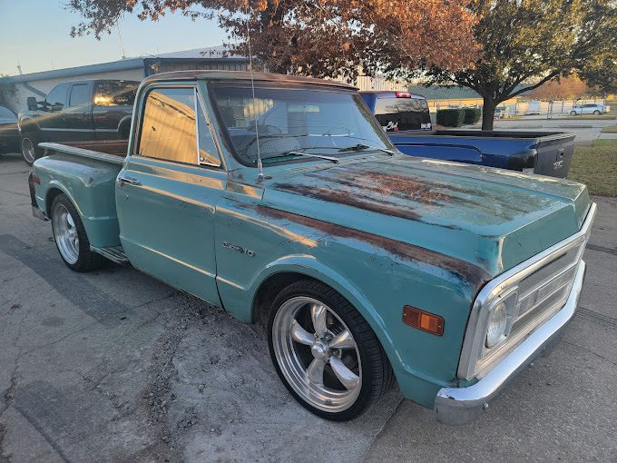 A teal classic Chevrolet pickup with patina and polished wheels parked in a gravel lot