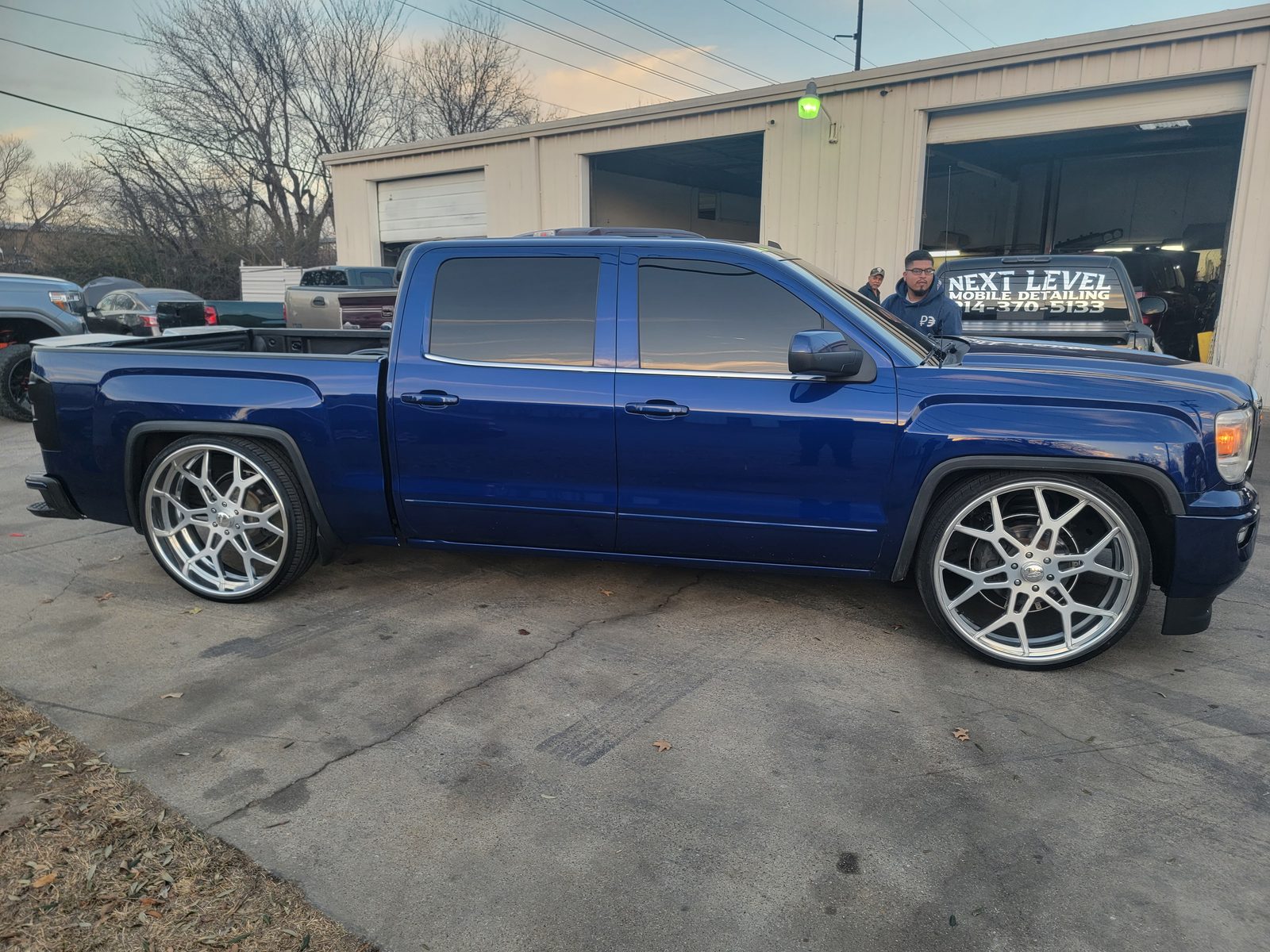 A lowered blue GMC pickup with large chrome wheels parked outside a commercial shop building