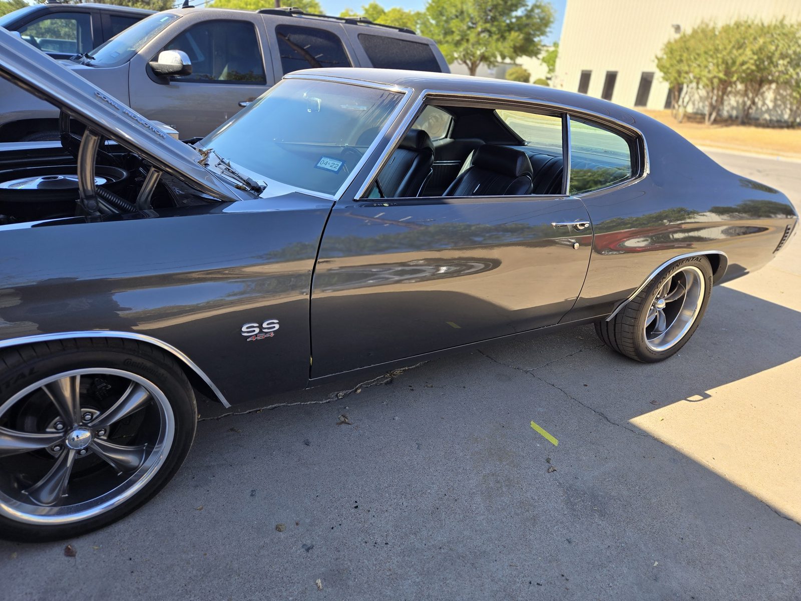 A gray classic Chevrolet Chevelle SS with its driver door open, parked outside on a sunny day
