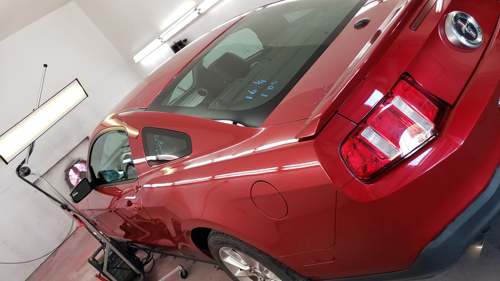 The rear quarter and tail lamp of a red Ford Mustang inside a bright white work area