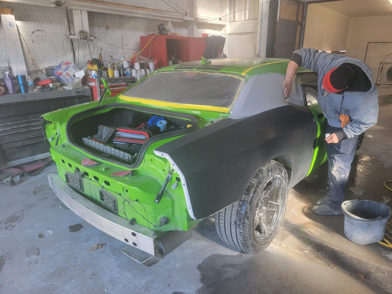 A technician working on a lime green Dodge Challenger with dark primered body panels inside the shop bay